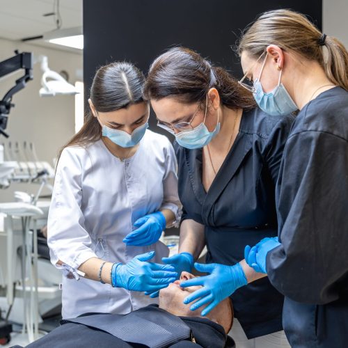 Team of female dentists treating patient's teeth. Visit to the dentist. Dentistry. High quality photo. Dentists in rubber gloves and medical masks on their faces. Dental office.